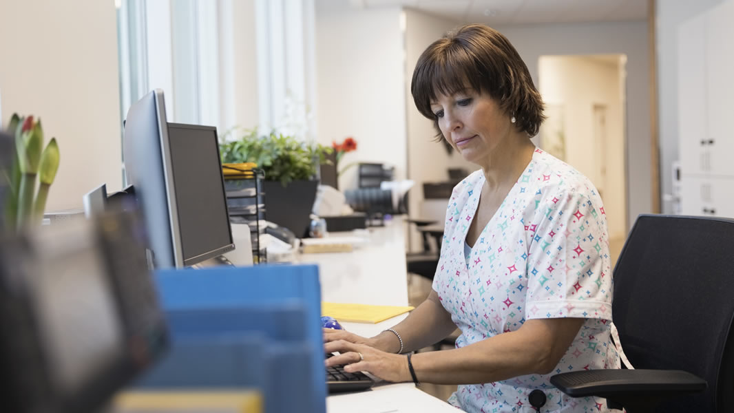 Female nurse typing at computer at clinic nurses station